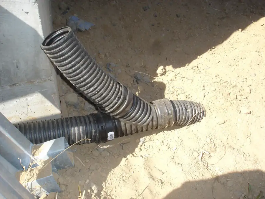 Corrugated drain pipe and wye fitting running alongside a concrete foundation edge